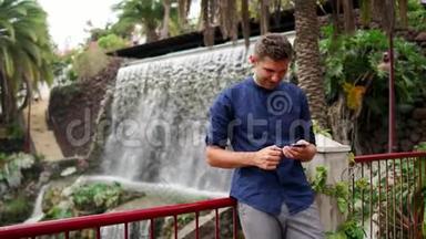一个穿着衬衫的人站在瀑布附近，在智能手机上写着一条信息。 智能手机远程工作